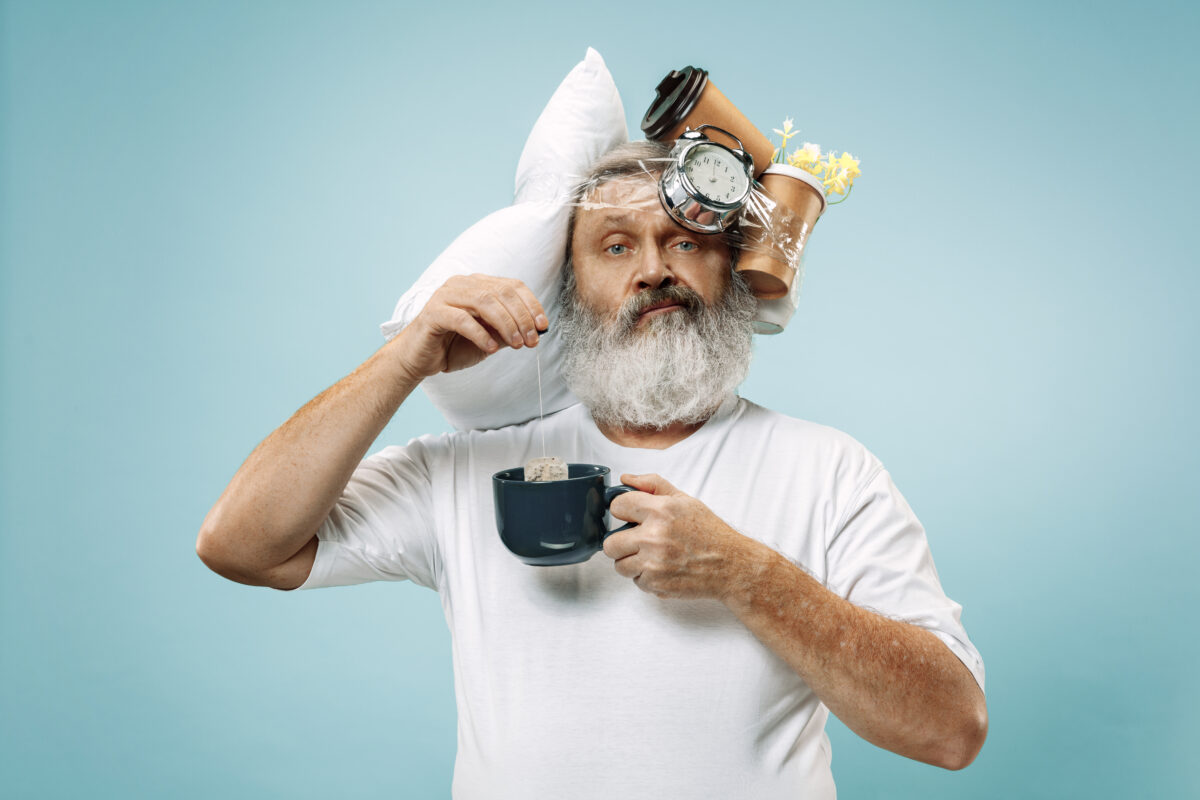 Tired man sleeping at home having too much work. Bored businessman with pillow and hourglass