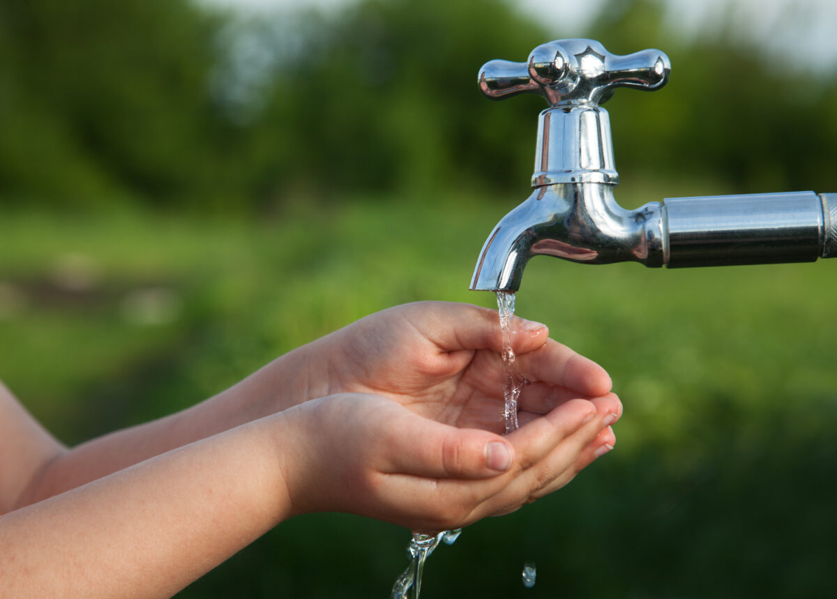 boy washes his hand under the faucet in garden